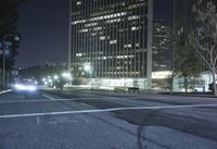 a view of the street at night in front of the city lights and buildings, looking toward one of two street lights