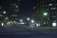 a view of the street at night in front of the city lights and buildings, looking toward one of two street lights