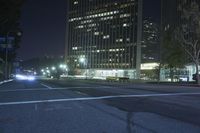 a view of the street at night in front of the city lights and buildings, looking toward one of two street lights