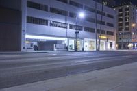 a street at night with empty sidewalks next to an apartment building and trees in the background