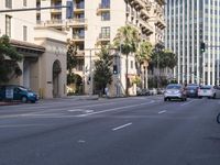 a city street with many cars going down it and buildings on the other side and some palm trees