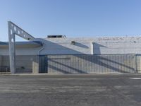 a long building has two windows and is near an entrance with a gate and blue roof