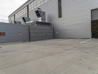 a large grey hangar with lots of windows in front of the building by itself in a parking lot