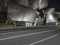 a view from the side of a street at night with an abstract building on it