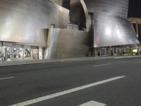 a view from the side of a street at night with an abstract building on it