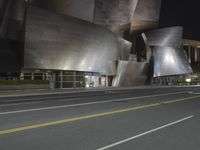 a view from the side of a street at night with an abstract building on it