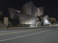 a view from the side of a street at night with an abstract building on it