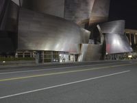 a view from the side of a street at night with an abstract building on it