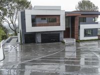 a large home in the rain with two cars parked outside it and one of the garages is covered with water