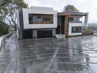 a large home in the rain with two cars parked outside it and one of the garages is covered with water