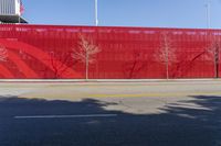 a red building with a wall made out of metal bars and some trees in front