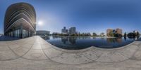 the circular object is on the side of a river and reflecting in the water, with a skyline in the background