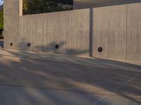 a skateboarder is riding an empty concrete court as seen from the street side