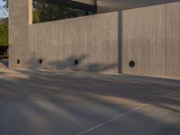 a skateboarder is riding an empty concrete court as seen from the street side