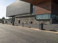 the large building is next to the walkway near a road leading to a building with a metal fence