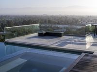 the patio with an infinity pool overlooks a city below it and a bench near to the water