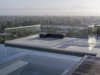 the patio with an infinity pool overlooks a city below it and a bench near to the water