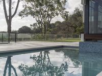 the reflection of a tree on a pool with an outdoor patio and lounge area around it