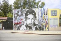 large mural depicting a portrait of prince and holding a cigarette in a street corner with buildings