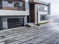 a paved stone pathway leads into a modern house with a gray wall and balcony railing