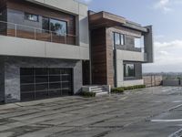 a paved stone pathway leads into a modern house with a gray wall and balcony railing