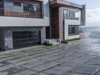 a paved stone pathway leads into a modern house with a gray wall and balcony railing