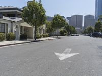 an arrow is painted on the side of a street in a city with tall buildings and parked cars