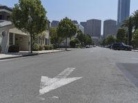 an arrow is painted on the side of a street in a city with tall buildings and parked cars