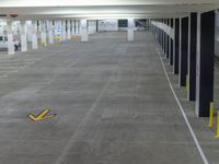 an empty parking garage with a yellow arrow pointing at the floor of the area where there is another car