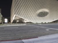 the view of an architecturally designed building at night from across the street from a pedestrian crossing