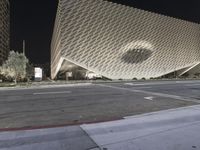 the view of an architecturally designed building at night from across the street from a pedestrian crossing