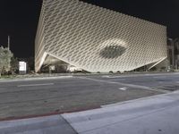 the view of an architecturally designed building at night from across the street from a pedestrian crossing