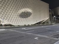 the view of an architecturally designed building at night from across the street from a pedestrian crossing