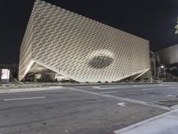 the view of an architecturally designed building at night from across the street from a pedestrian crossing