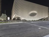 the view of an architecturally designed building at night from across the street from a pedestrian crossing