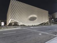 the view of an architecturally designed building at night from across the street from a pedestrian crossing