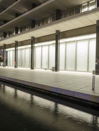 the empty sidewalk outside a building on the water front at night with buildings around it