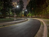 a quiet empty roadway with trees and lighting on at night time in the city area