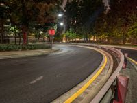 a quiet empty roadway with trees and lighting on at night time in the city area