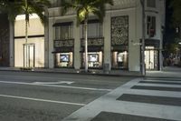 a tall white building sitting next to two trees in the city street at night with a crosswalk