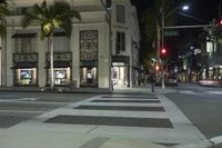 a tall white building sitting next to two trees in the city street at night with a crosswalk