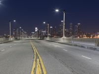 a city skyline seen across the bridge of a river at night, with street lights shining above the street