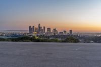 the view of city with skyscrapers from an empty parking lot at sunset time with light coming on in the distance