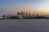 the view of city with skyscrapers from an empty parking lot at sunset time with light coming on in the distance