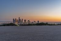 the view of city with skyscrapers from an empty parking lot at sunset time with light coming on in the distance