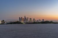 the view of city with skyscrapers from an empty parking lot at sunset time with light coming on in the distance