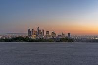 the view of city with skyscrapers from an empty parking lot at sunset time with light coming on in the distance