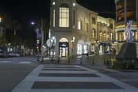 a crosswalk that has a statue in front of it at night time in front of several buildings and shops