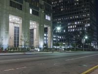 a street with parked cars at night near a tall building with multiple columns in the background