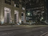 a street with parked cars at night near a tall building with multiple columns in the background